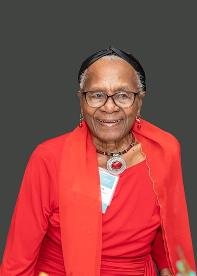 A closeup of a old woman, she smiles at the camera, she has long short and has a red dress on